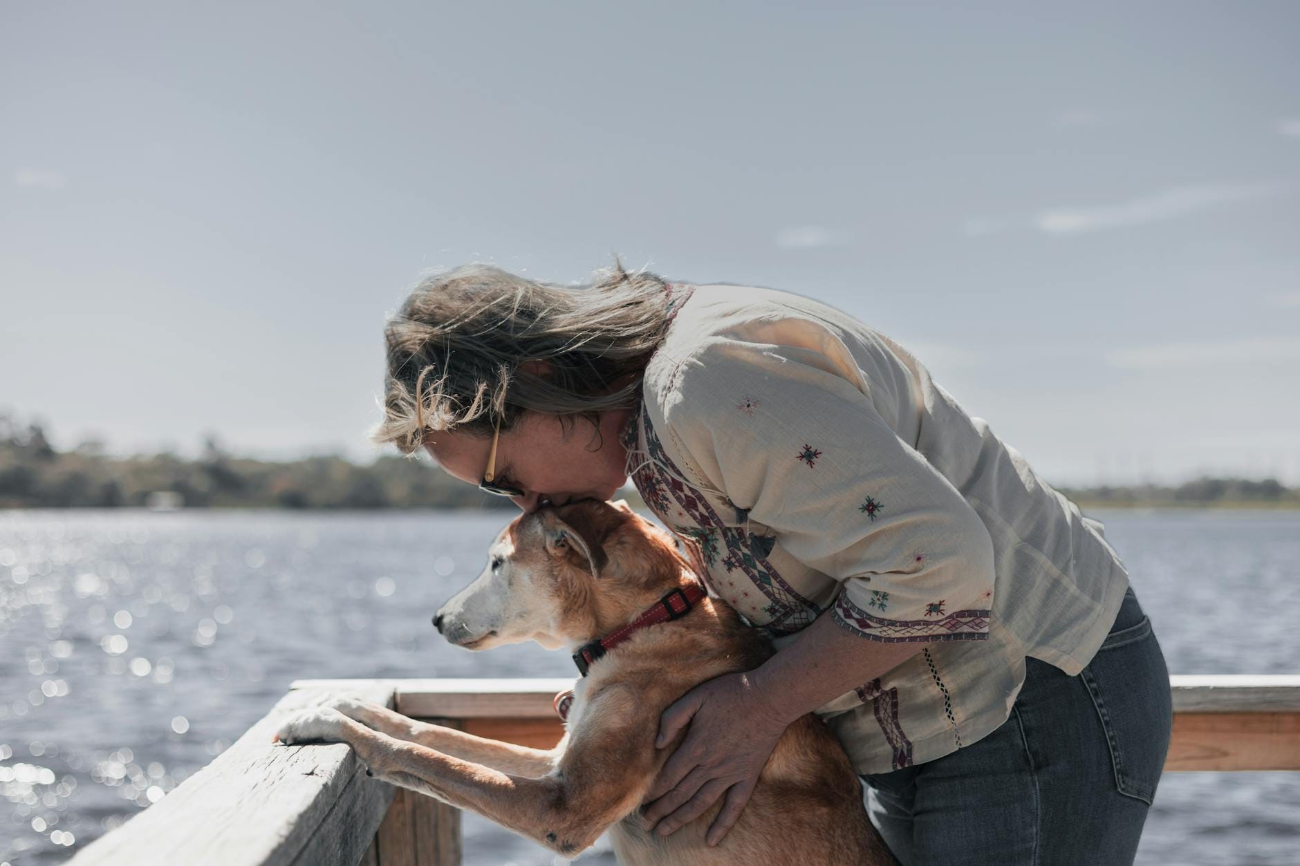 Kobieta przytula psa nad brzegiem jeziora latem